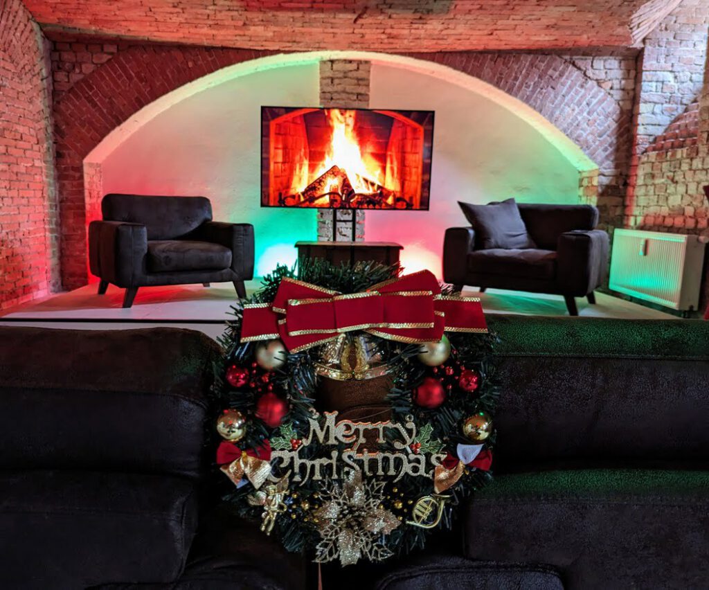 Weihnachtliche Bühne im TMPL Studio mit zwei Sesseln, LED-Feuerhintergrund und dekoriertem Kranz mit der Aufschrift "Merry Christmas".